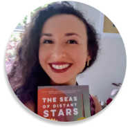 Francesca Varela smiling and holding up a copy of her third novel, The Seas of Distant Stars.