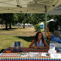 Francesca Varela sitting at a table outside, selling books.