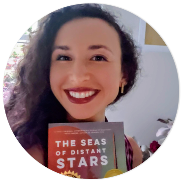 Francesca Varela smiling and holding up a copy of her third novel, The Seas of Distant Stars.