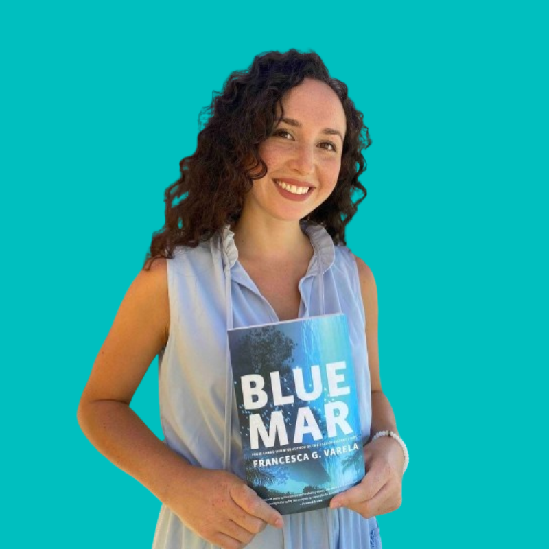 Author, nature writer, and copy editor Francesca Varela holding up a copy of her book, Blue Mar, in front of a blue background